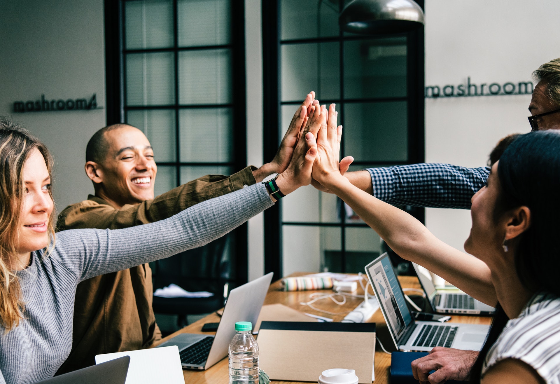 Cheesy photo of four people around a table doing a group high five.